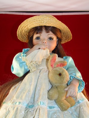 Identifying a Porcelain Doll - doll with a hanky to her nose, wearing a straw hat and blue satin dress with eyelet bodice and skirt, holding a stuffed bunny