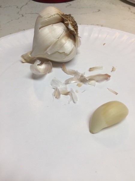 A bulb of fresh garlic with one peeled clove.