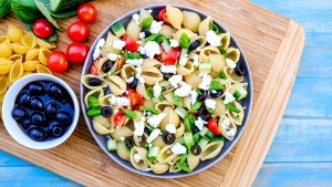 A bowl of Greek pasta salad with tomatoes, olives and feta cheese.