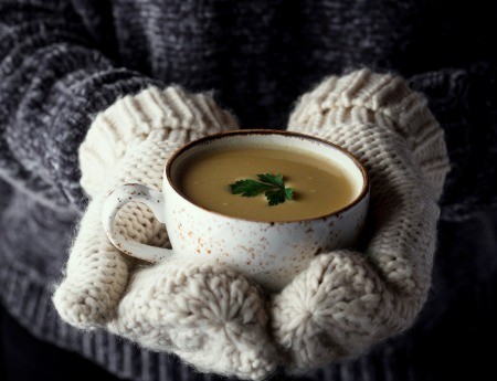 A pair of mittened hands holding a cup of soup.