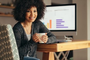 A woman with a coffee cup and a computer monitor behind her.