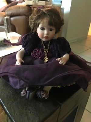 Identifying a Porcelain Doll - sitting doll wearing a dark purple dress and gold chain with a heart shaped pendant