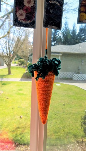 Crocheted Carrot - carrot hanging below a seed packet garland in the window