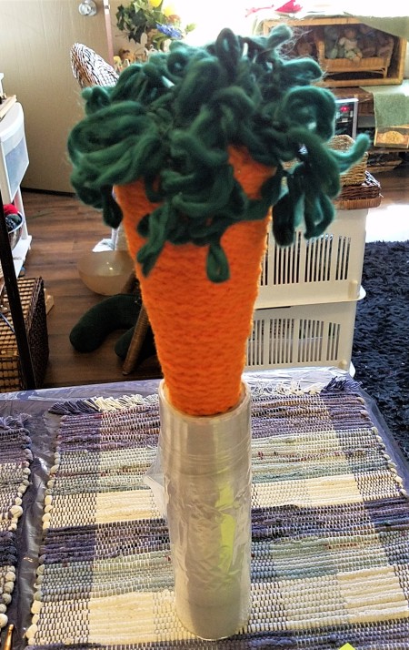 Crocheted Carrot - finished carrot standing in a roll of plastic