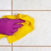 A gloved hand cleaning a tile surface.