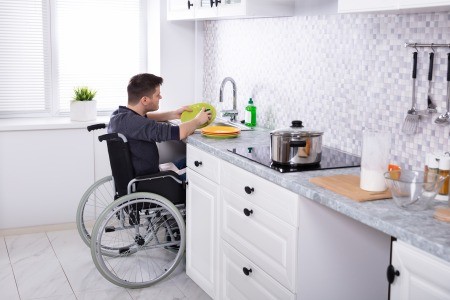 A man in a wheelchair doing the dishes.
