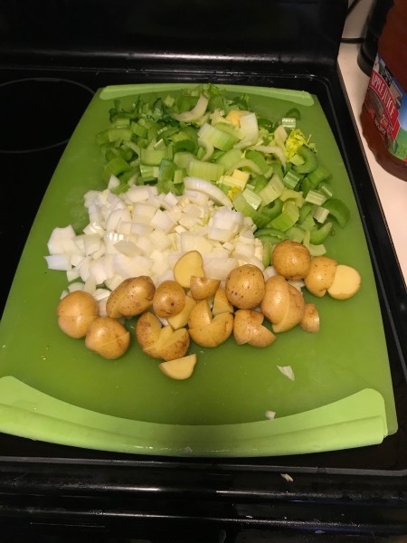 Celery, onion and potatoes chopped on a cutting board.