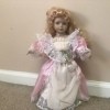 Identifying a Vintage Porcelain Doll - doll wearing a pink dress with a white pinafore leaning up against a wall