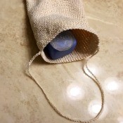 Crocheted Exfoliating Soap Sack - sack with a piece of soap inside lying on the bathroom counter