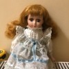 Identifying a Porcelain Doll - doll wearing a white dress trimmed with lace and blue ribbon