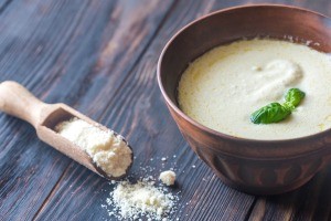 A bowl of alfredo sauce next to a scoop of parmesan.