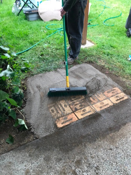 Using a broom to brush the sand into the cracks.