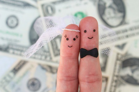 Two fingers decorated as a bride and groom with a background of dollar bills.