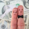 Two fingers decorated as a bride and groom with a background of dollar bills.