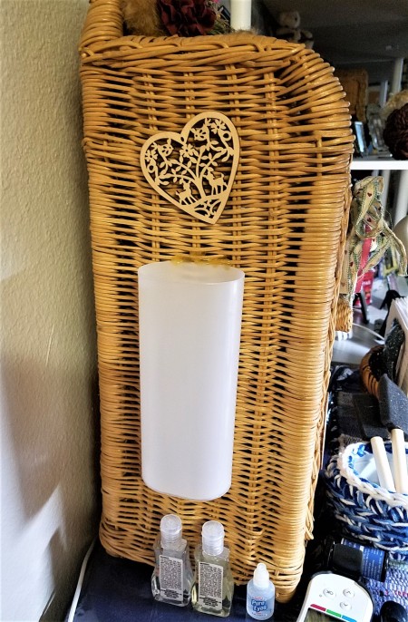 A plastic container attached to the side of a small wicker shelf.