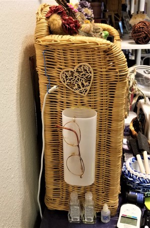 Eyeglasses hanging on a plastic container attached to the side of a small wicker shelf.