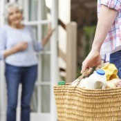 A woman delivering a shopping basket full of groceries to a neighbor.