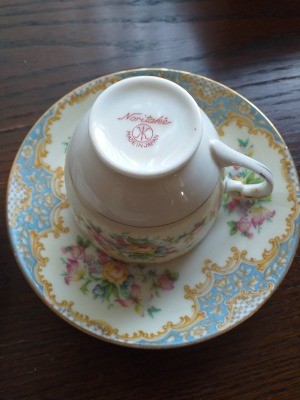 Value of Noritake China - upside down cup on a heavily decorated saucer with blue and brown design around the edge and clusters of pink flowers in three areas in between
