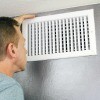 A man looking at an air vent.