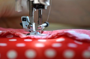 A sewing machine needle sewing a seam in red and white polka dotted fabric.