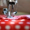A sewing machine needle sewing a seam in red and white polka dotted fabric.