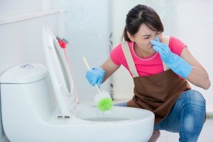 A woman cleaning a stinky toilet.