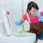 A woman cleaning a stinky toilet.