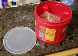 A recycled coffee container with a plastic lid next to it.