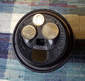 Coins on top of a paper cup with a plastic lid.