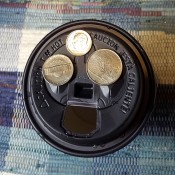 Coins on top of a paper cup with a plastic lid.