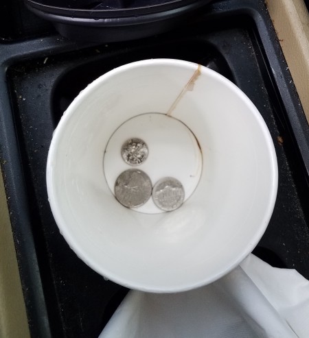 Coins in the bottom of a recycled paper cup.
