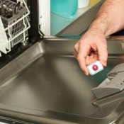 A person putting soap in a dishwasher.