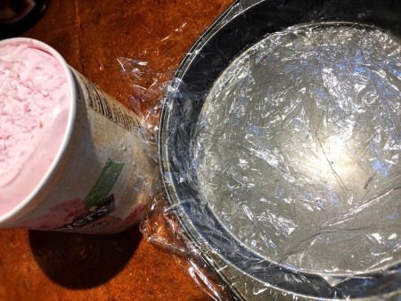 Cling wrap inside a round metal cake pan.