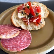 A plate with a slice of bread, topped with tomato, basil and garlic topping.