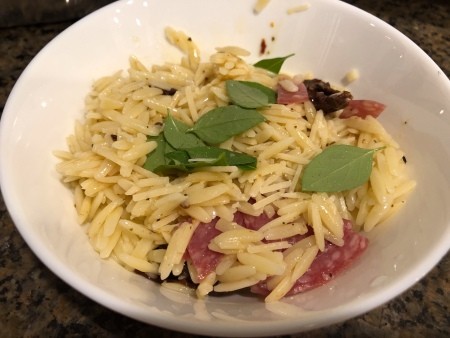 Basil being added to the orzo mixture.