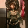 Identifying a Porcelain Musical Doll - doll with dark green and tan Victorian style dress and matching large hat, standing next to a computer monitor