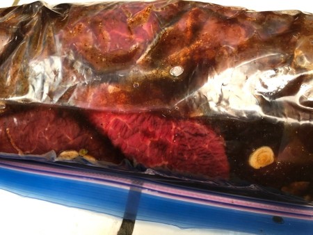 Steaks being marinated in a plastic ziplock bag.