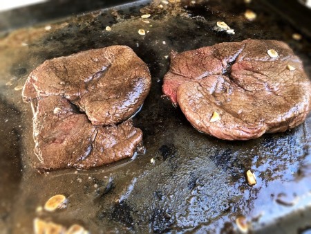 Marinated steaks being grilled on a cast iron griddle.