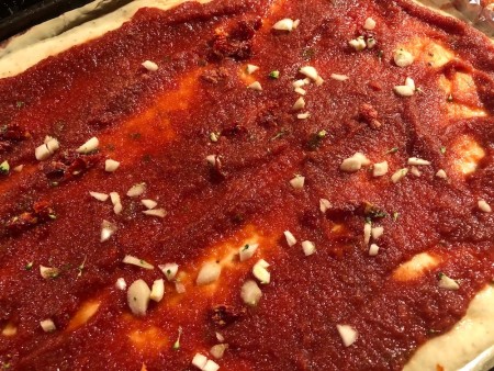 Adding minced garlic & dried tomatoes to pizza crust.