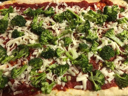 spreading broccoli on pizza.