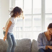 An angry girl jumping up and down on the couch with an upset mom sitting nearby.