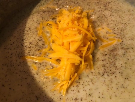 Melting cheddar cheese into soup pan.