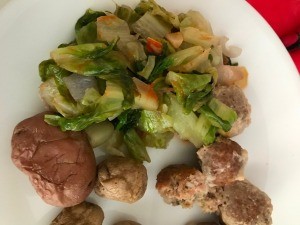 A dinner plate containing potatoes, meatballs and sauteed lettuce.