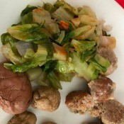 A dinner plate containing potatoes, meatballs and sauteed lettuce.