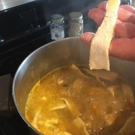 Adding homemade noodles to the soup pot.