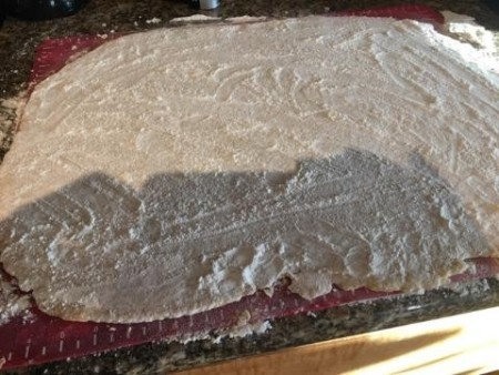 The noodle dough rolled out on a floured surface.