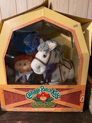 A Cabbage Patch doll and a stuffed horse in a box.
