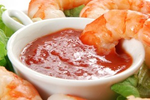 A dish of cocktail sauce surrounded by shrimp.