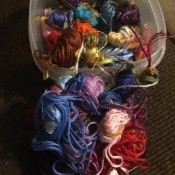 Several skeins of embroidery floss in a plastic container.
