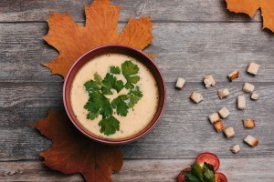 A bowl of pumpkin soup with autumn leaves underneath.